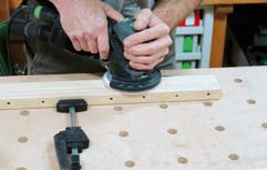 Damit das Dübelloch mittig im Querholz platziert werden kann, wird ein Leistenanschlag von vorne auf die Klappe geschoben.