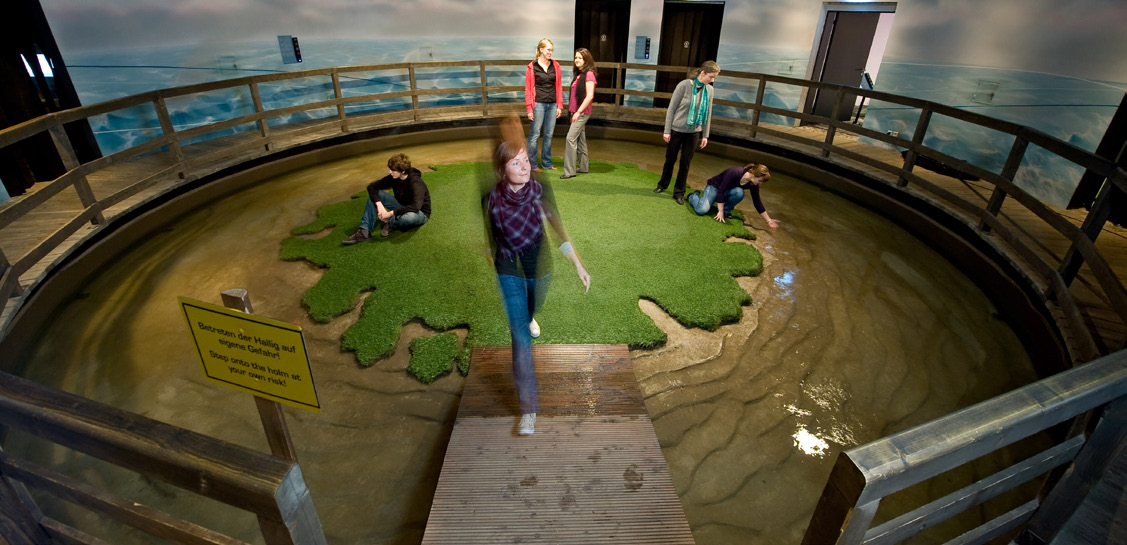 LANGENESS In der Mitte des Hauptraumes liegt umgeben von Wasser eine kleine Hallig, auf die der Besucher über einen Steg gelangt. Alle 12 Minuten findet hier eine Land-Unter-Inszenierung statt.