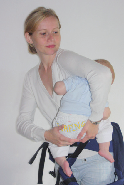 Rückenpaneel zwischen Babys Beinchen auf Babys Rücken hinauf klappen, sodass das Baby auf der Stegverkleinerung sitzt.