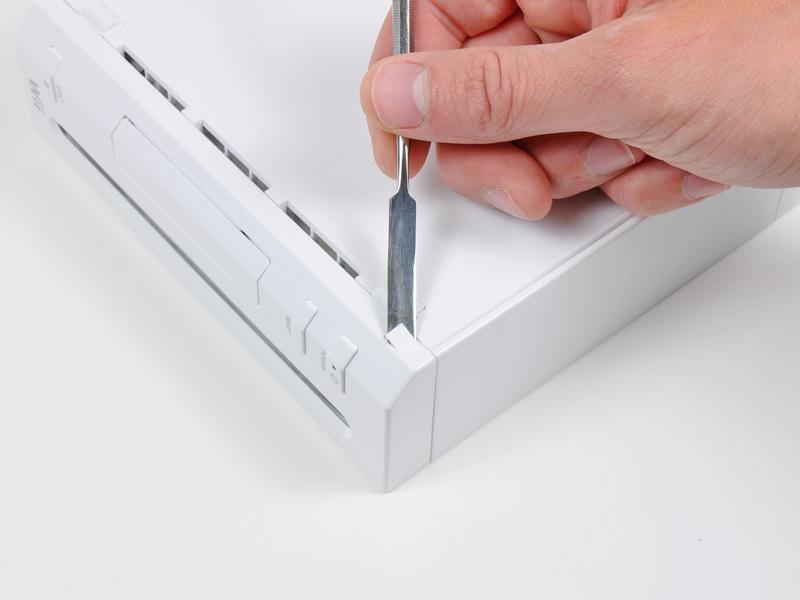 Schritt 1 Faceplate Verwenden Sie ein Metall spudger die weiße Kunststoff-Schraubenabdeckungen an dem unteren Gehäuse in der Nähe der Vorderseite der Wii stecken zu