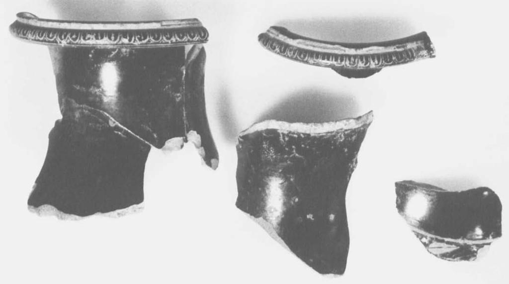 Figürliche Verzierung: erhalten sind Teile des Stockes in der Hand des Mannes im Bild links aufien, Teile des Peplos der Frau in der Mitte, Teile ihrer Hànde, die links eine Phiale, rechts eine Kanne