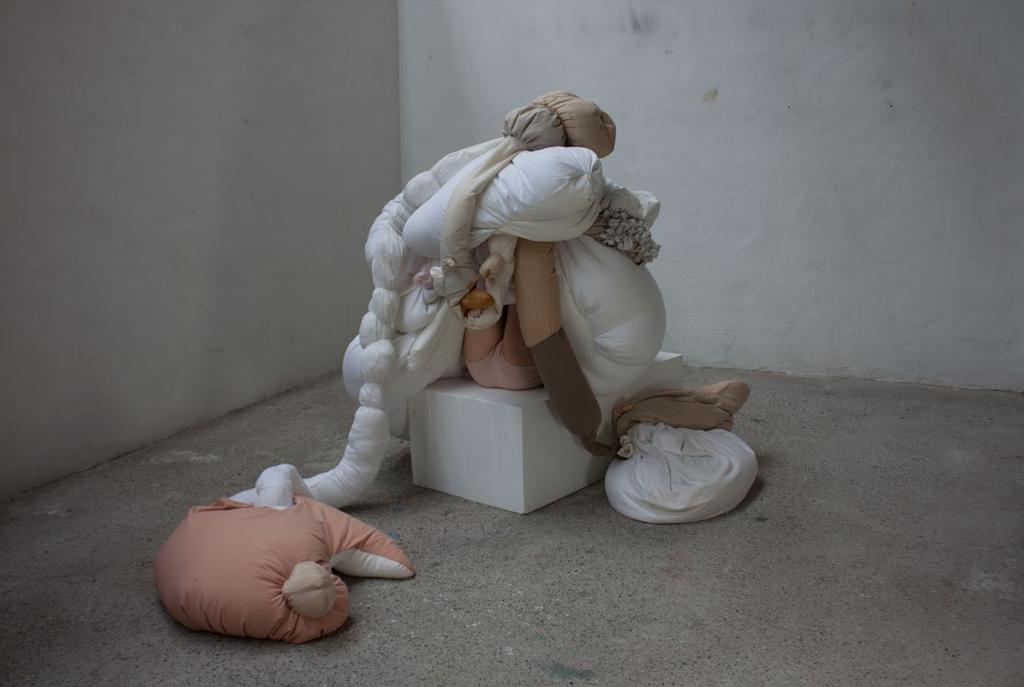 Ein menschlicher Körper und eine textile Skulptur agieren in einem neutralen Raum miteinander.