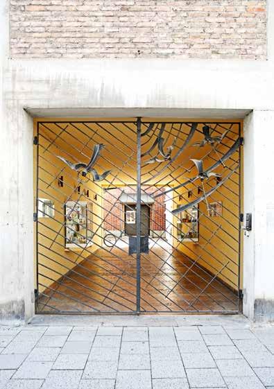 Durch das Eisengitter mit den apokalyptischen Engeln, gestaltet von Herbert Altmann, blickt man auf die ziegelsichtige Backsteinfassade.