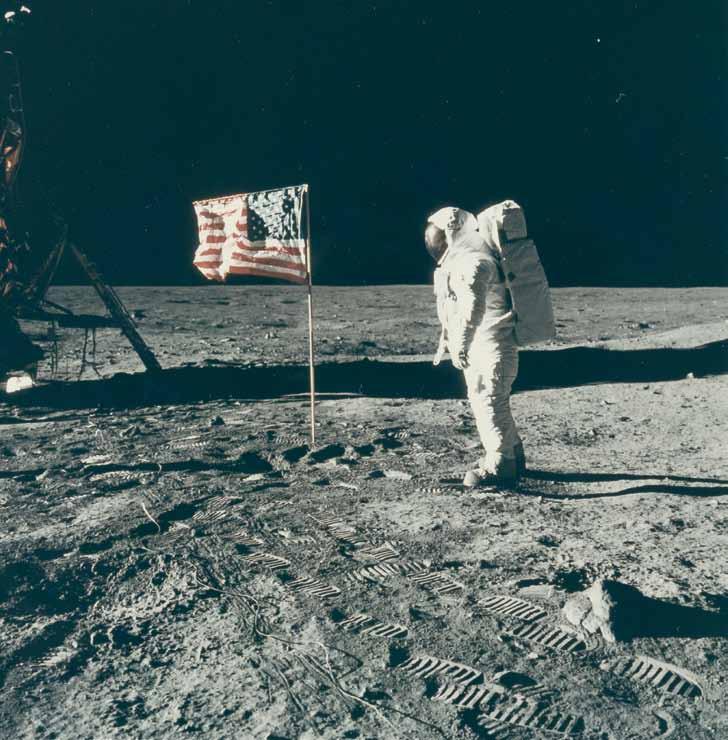 Space Oddity 1501 Neil Armstrong neben der aufgestellten Flagge. Links im Hintergrund ist die Mondlandefähre teilweise noch sichtbar. Der Vordergrund ist bedeckt mit den Fußspuren der Astronauten.