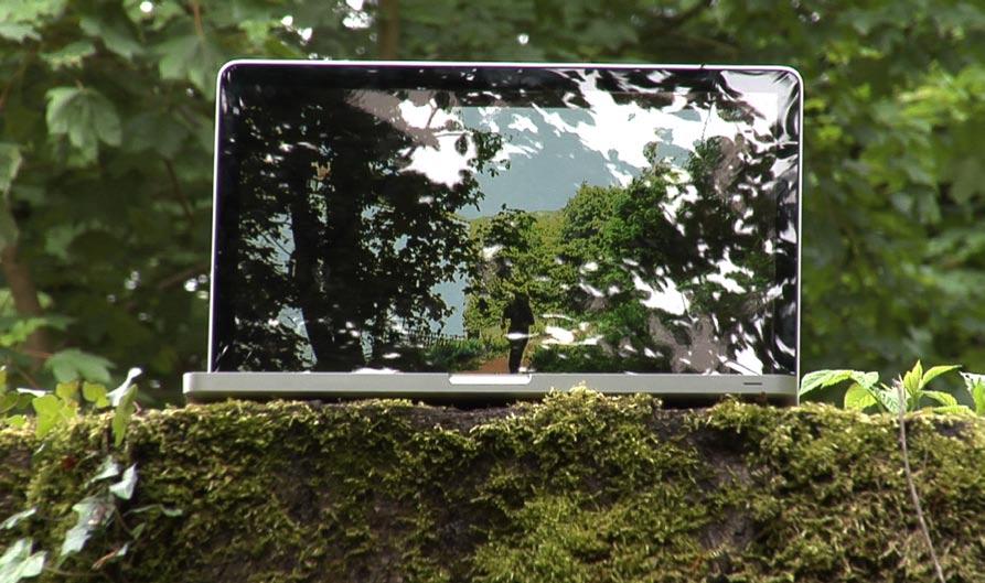 VIRTUAL AUTHENTIC DVCPRO HD, PAL, 2`00, 2010 für Flatscreen, 16 zu 9 Ein Laptop steht im Wald und zeigt ein Video derselben Umgebung.