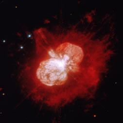 Die den Spitzen entsprechenden chemischen Elemente sind eingezeichnet. Bild 3. Falschfarbendarstellung des Sterns Eta Carinae, in der Mitte verdeckt. Er stieß vor ca.
