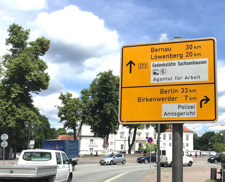 Ein Verkehrsschild verbindet in Oranienburg Hinweis auf Gedenkstätte Sachsenhausen mit Standort der Agentur für Arbeit.