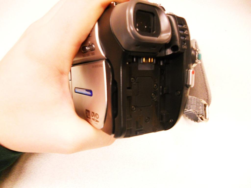 Drücken Sie den kleinen Knopf auf der Unterseite der Kamera, mit dem roten Kreis markiert, dann schieben Sie den gesamten Schalter nach vorne, mit dem