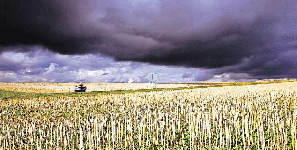 Dicke Wolkenziehen übereinem abgeernteten Getreidefeld auf. Unwetter undstarkregen gibt es,bedingt durch denklimawandel, immerhäufiger.