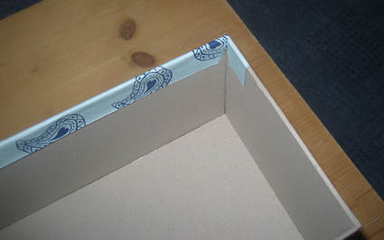 Foto 2 zu Schritt 3 Das kleinere Teil des überstehenden Papiers (Richtung Schachtelboden) wird jetzt auf die untere Seite der Schachtel