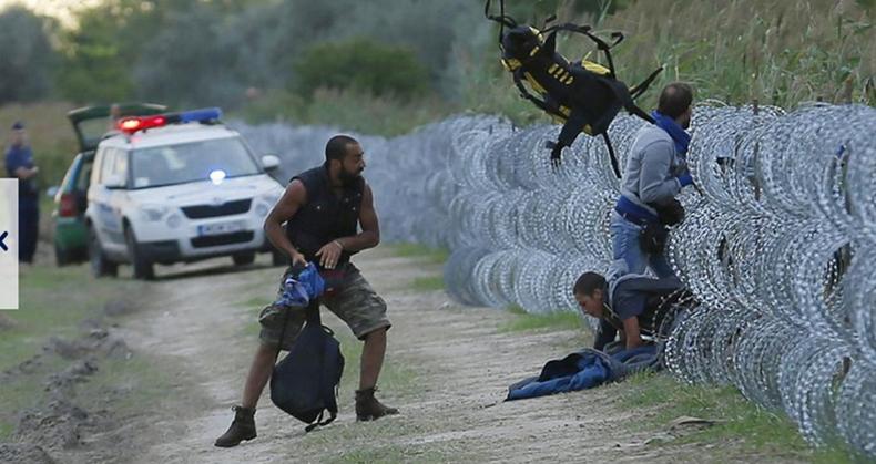8 (Das wenige Gepäck, das die Flüchtlinge dabei haben, wird hinterhergeworfen. Dieser syrische Flüchtling fängt den Rucksack seines Freundes auf, während die ungarische Grenzpolizei zuschaut.