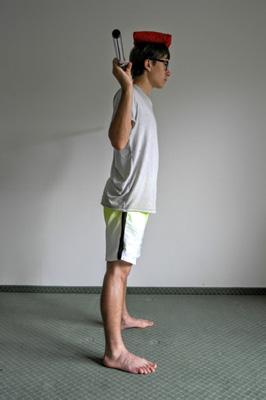 2 Während Durchführung einer Kniebeuge balanciert Übende einen Sandsack auf dem Kopf.