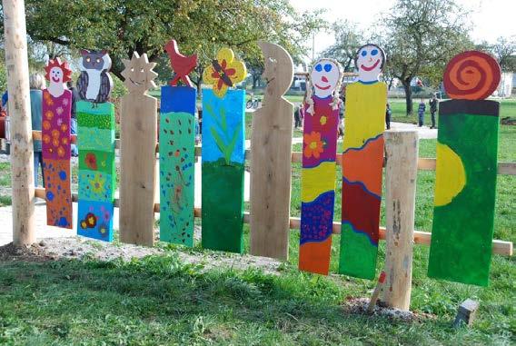 Spatenstich für den neuen Kinderspielplatz Holzfiguren mit lustigen Gesichtern, Sonne und Mond, eine Schnecke und ein Schmetterling, Igel, Eule und andere und bunt bemalte Bewohner der Streuobstwiese
