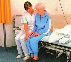 Die Pflegekraft macht der Patientin vor dem Aufstehen durch Druckausübung in Richtung Boden deutlich, dass sie ihr Gewicht auf die Füße verlagern kann.