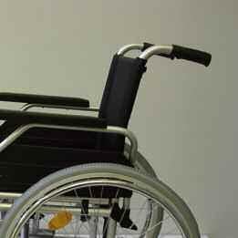 Der obere Helfer hält den Rollstuhl an den Schiebegriffen, sichert ihn und hält ihn in der richtigen Position. Der Rollstuhl soll Stufe für Stufe herunterrollen.