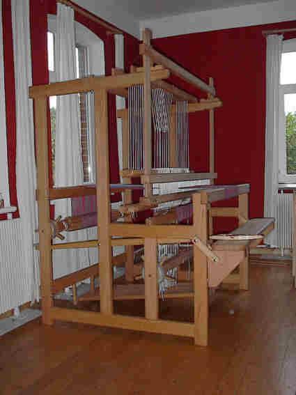 Der Flachwebstuhl MALMÖ ist ein kompakter Webstuhl, der sich durch einen geringen Platzbedarf auszeichnet. In der Standardversion besitzt er einen Rollenzug mit vier Schäften und sechs Tritten.
