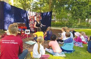 Stichpunkte 25 Stiftung Berlin-Spandau Begeisterte Kinder beim Lesen im Park Strahlender Sonnenschein, Sitzkissen unter schattenspendenden Bäumen, Girlanden mit bunten Bildern.