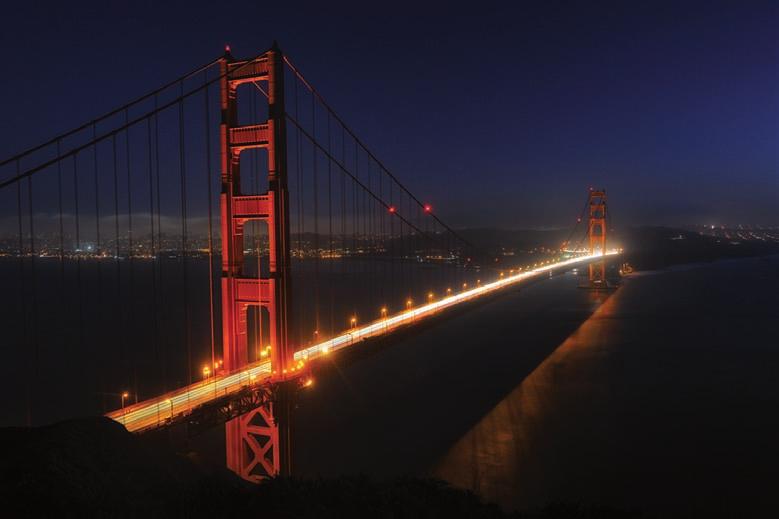 Abends erleuchten künstliche Lichtquellen die Golden Gate Bridge erneut und hellen das Rot der Brücke auf.
