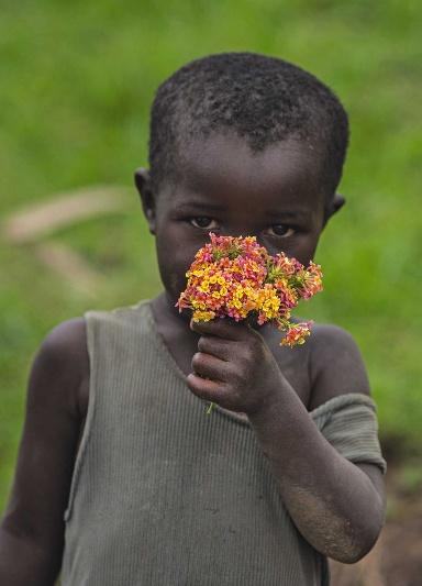 28 Ein Batwa-Mädchen riecht an Blumen, die es auf einer der vielen kleinen Inseln im Bunyonyi-See gepflückt hat.